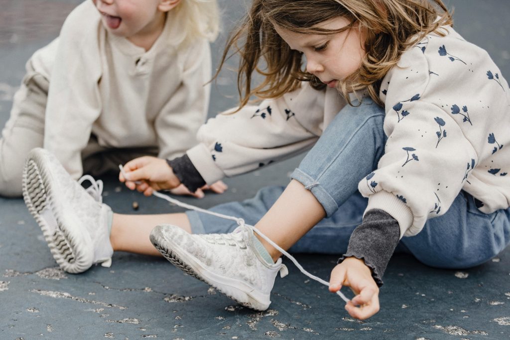 A young girl sits outdoors tying her shoelaces, enjoying a carefree moment.