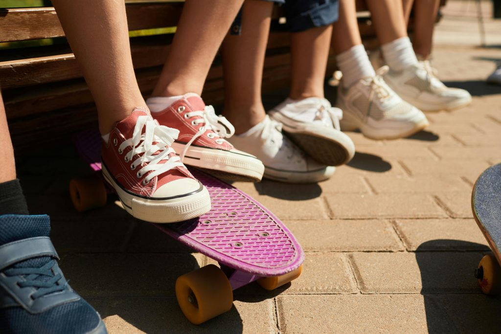 Close-up of children's feet in sneakers with skateboards in a sunny park.